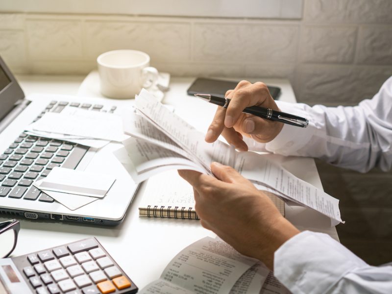 A business man holding pen while looking at the bills in his workplace. Business concept.