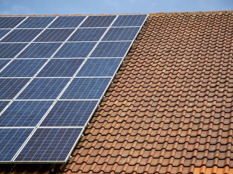 solar panels on roof of house. horizontal orientation, blue sky, gray panels on brown roof.