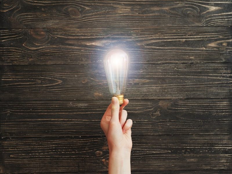 Hand holding light bulb on wooden board