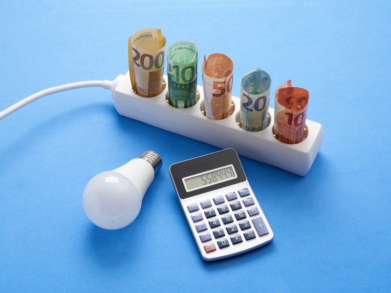 Electric power strip with banknotes on blue background with a light bulb and a calculator, concept spending and saving electricity